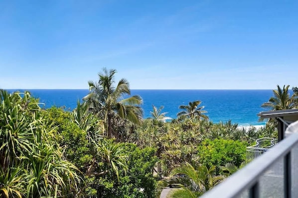 A balcony with a view of the ocean and tropical vegetation.