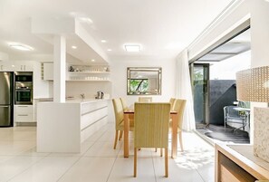 A modern kitchen with white cabinetry, a dining area with a central island, and a large window providing a view of the outdoors.