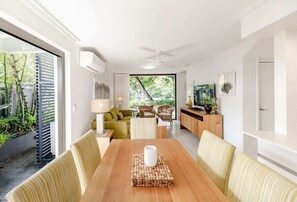 Un espace de restauration moderne avec une table en bois, des chaises rembourrĂ©es et une vue sur un jardin grĂące Ă de grandes fenĂȘtres.
