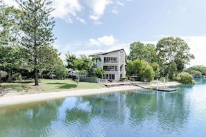 Une maison moderne Ă deux Ă©tages, situĂ©e au bord dâun lac paisible et dotĂ©e dâun quai, le tout entourĂ© dâune vĂ©gĂ©tation luxuriante.