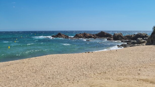 A beach with clear blue water, sandy shore, and rocky outcrops.