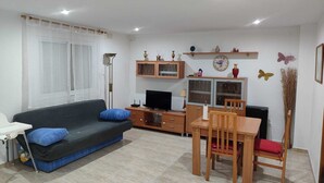 A living room with a sofa, TV, wooden cabinet, and a dining table with chairs.