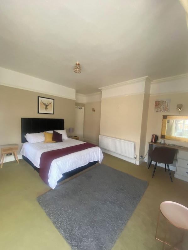 A bedroom with a bed, a desk, a chair, a radiator, and a small stool. - Stokesay inn and b and b (Craven Arms)