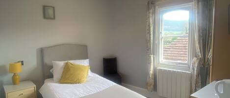 Una camera d'albergo con un letto, un comodino, una lampada, una finestra con tende e un bagno.