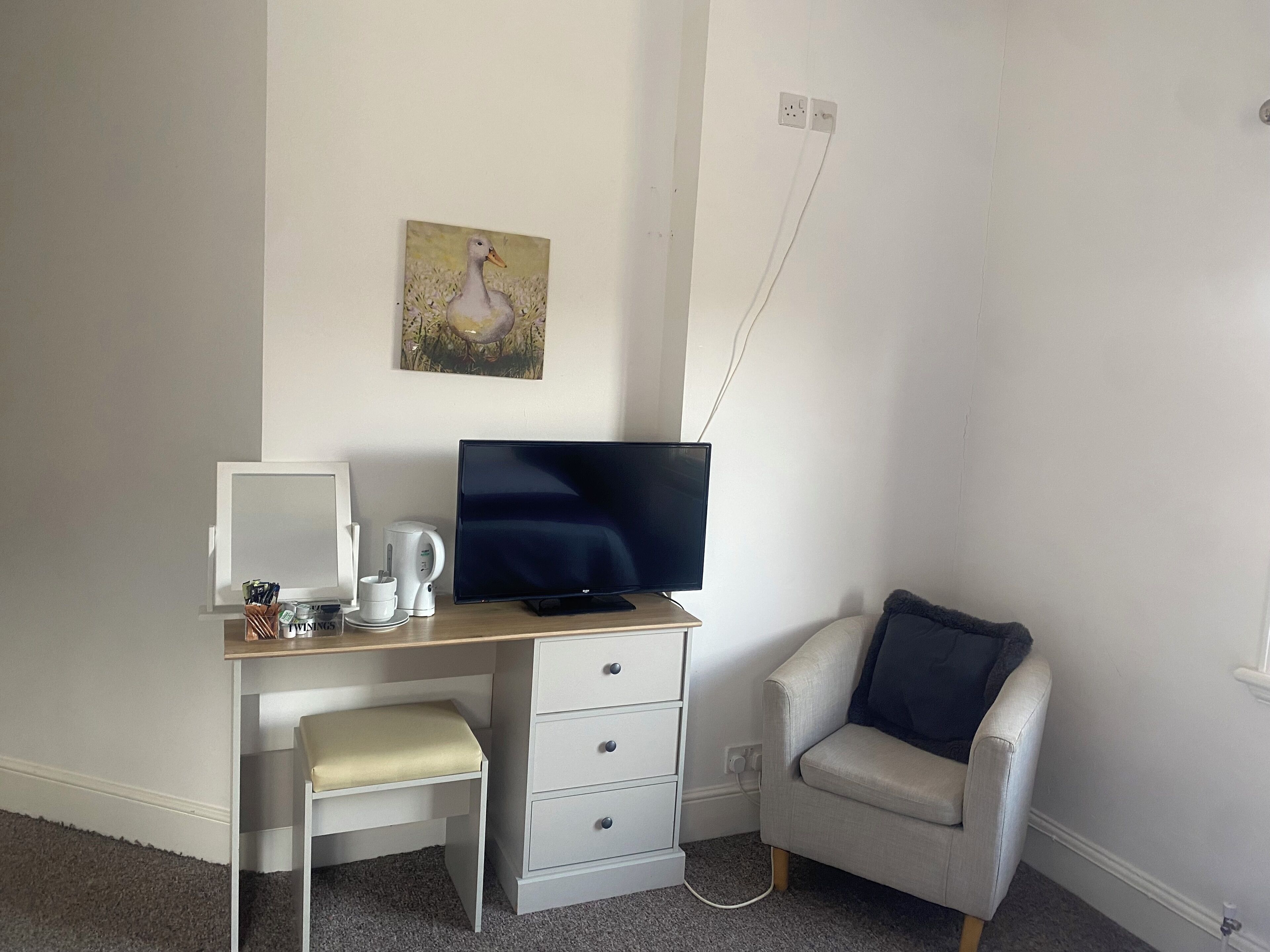 Ein kleiner, ordentlicher Raum mit Schreibtisch, Stuhl, Fernseher und einem Bild an der Wand.