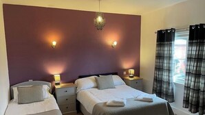 A hotel room with two beds, a large wall-mounted light fixture, and a window with plaid curtains. - Stokesay inn and b and b  (Craven Arms)