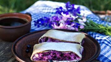 A wooden table with a plate of blueberry pancakes and a small bowl of syrup.