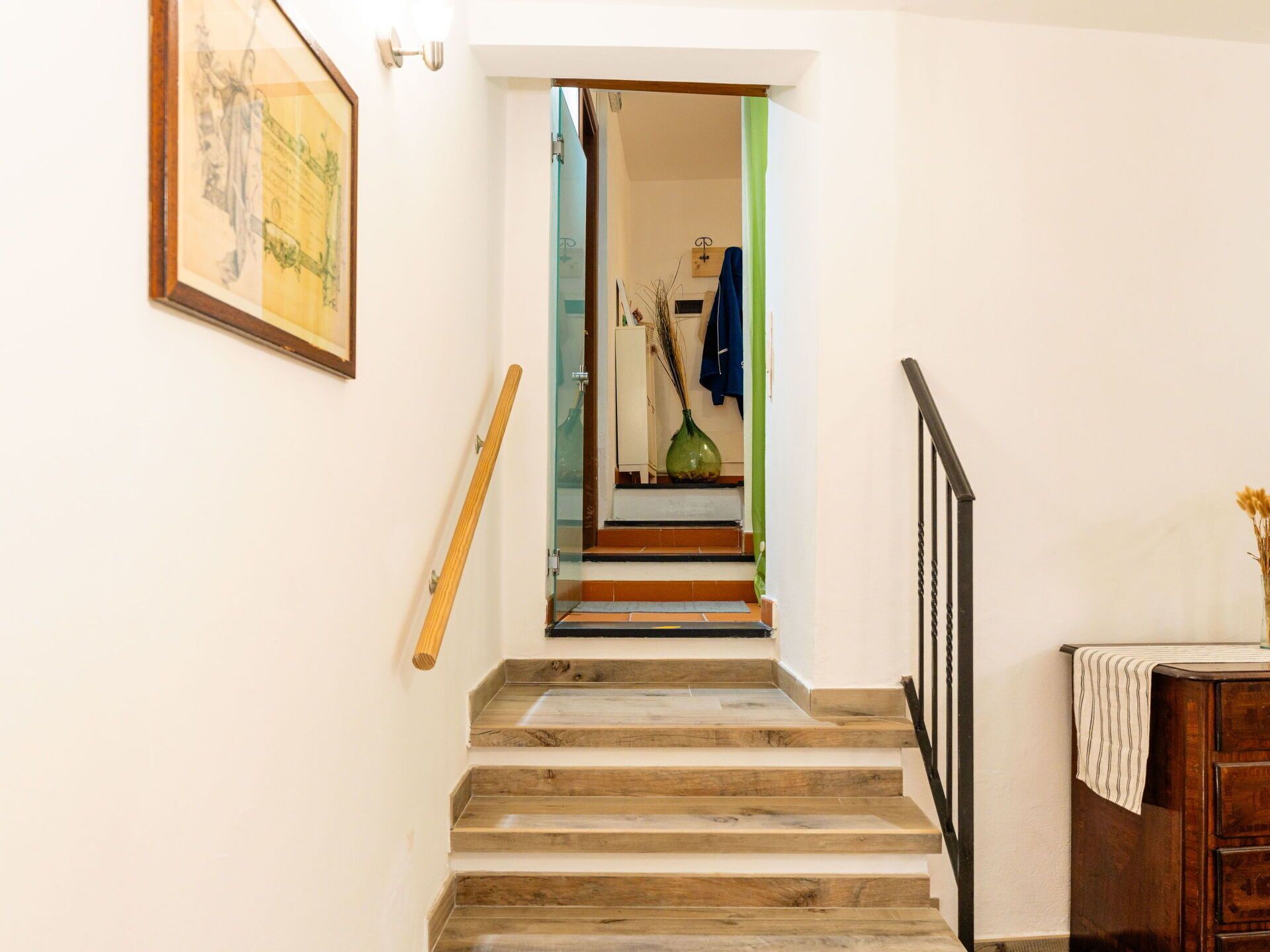 Uma escada de madeira com corrimão, que dá acesso a um quarto com uma cama e uma cômoda.
