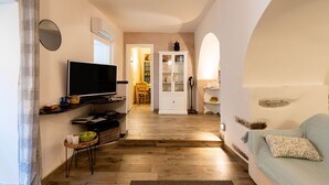 A living room with a TV, a sofa, a dining area, and a kitchen visible through an archway. - Cosy apartment for 4 guests with WIFI, A/C, TV and terrace (Chiesa)