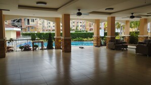 A spacious indoor area with tiled flooring, multiple ceiling fans, and a pool visible through a glass barrier.