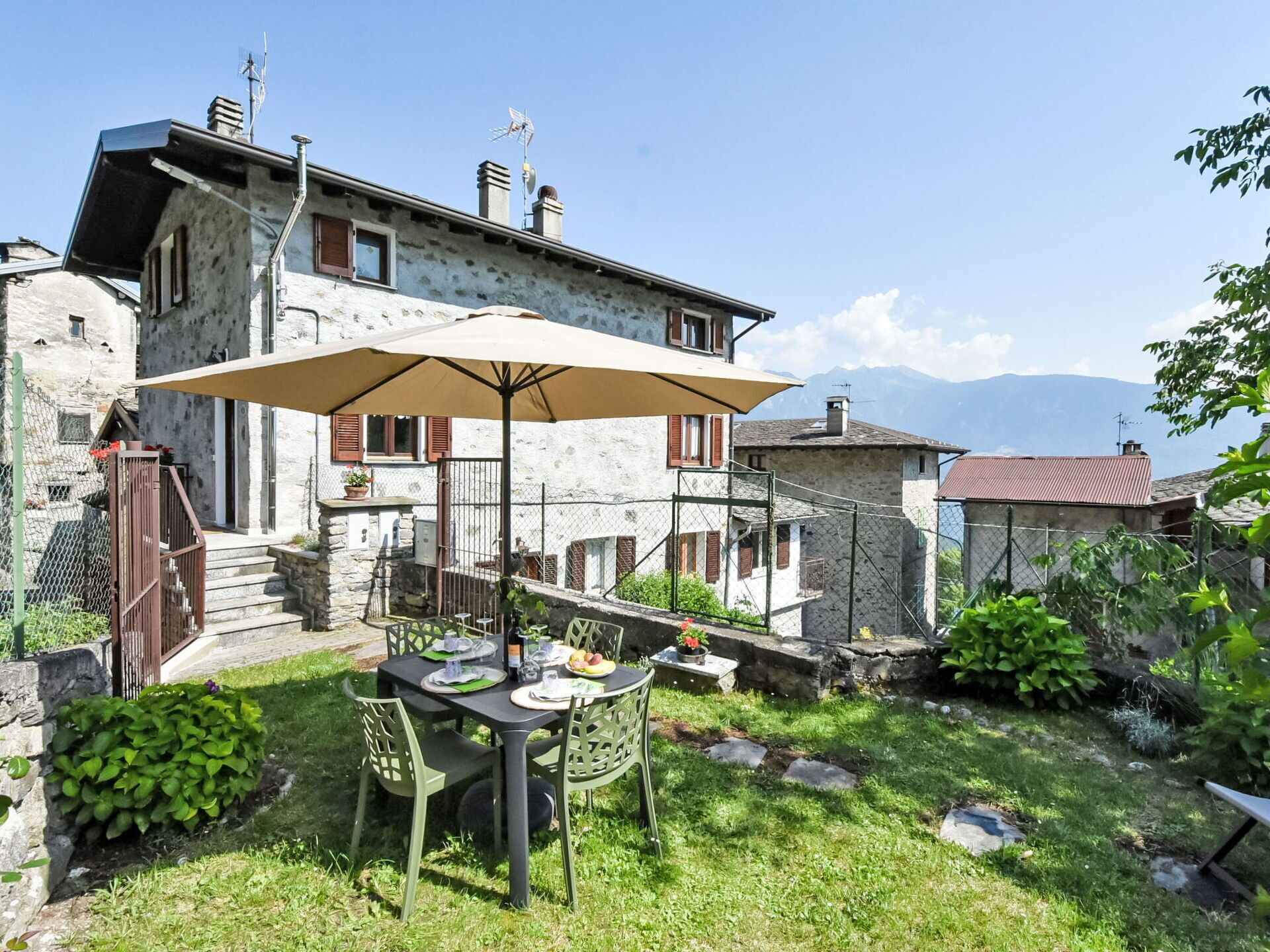 Une maison en pierre avec une table et des chaises sur une terrasse, entourée d’un mur de pierre et de verdure.