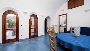 A room with a blue tiled floor, wooden doors with glass panels, a dining table with blue tablecloth, and a kitchen area with a microwave.