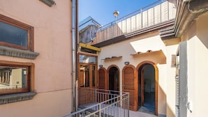 A narrow alleyway with a metal railing, wooden doors, and a small balcony.