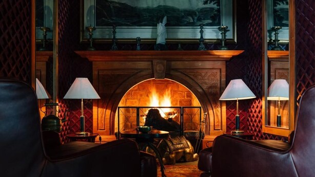 A cozy room with a fireplace, leather chairs, and a table with a lamp. - Sinhagiri Mansion (Nuwara Eliya)