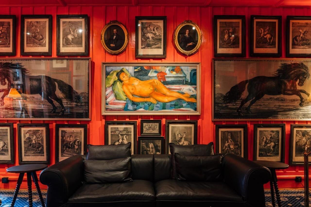 Ein Zimmer mit einer schwarzen Ledersofa, gerahmten Kunstwerken an den Wänden und einem großen Gemälde einer Aktfigur.