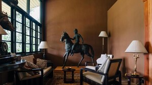 A cozy room with a large window, a statue of a rider on a horse, two chairs, a small table, and a lamp. - Sinhagiri Mansion (Nuwara Eliya)