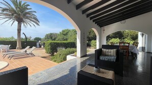 A covered outdoor seating area with lounge chairs, a table, and a sofa.