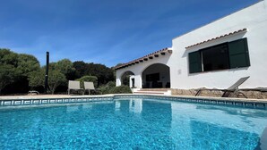 A clear swimming pool with lounge chairs and a white building with arches.