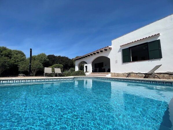 Une piscine aux eaux cristallines, dotée de chaises longues, et un bâtiment blanc orné d’arcades.