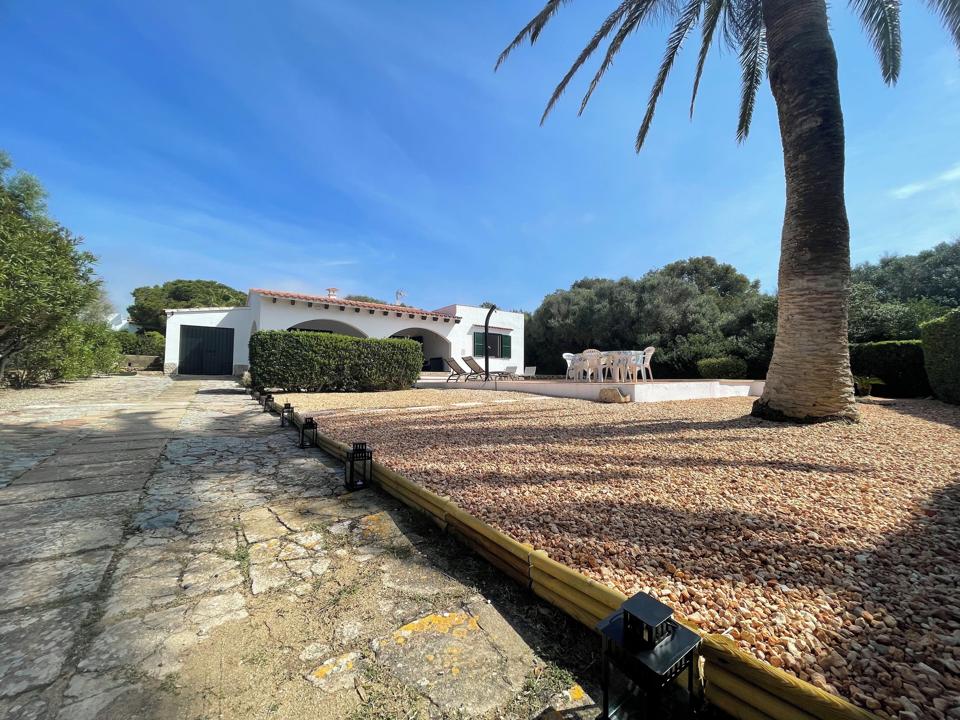 A courtyard with a palm tree, a white building with arches, and a seating area with chairs.