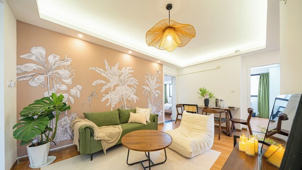 Un salon avec un canapé vert, un fauteuil blanc, une table basse en bois et une grande fresque murale.