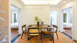Un coin repas avec une table en bois, quatre chaises, un vase avec des fleurs et, au fond, un lit.