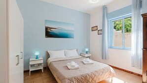 Un dormitorio con cama, dos mesitas de noche con lámparas, un cuadro en la pared y una ventana con cortinas.