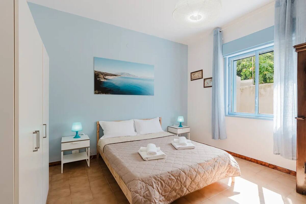 Une chambre à coucher avec un lit, deux tables de chevet avec des lampes, un tableau au mur et une fenêtre avec des rideaux.