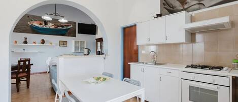 A modern kitchen with white cabinets, a gas stove, and a dining area with a white table and chairs.