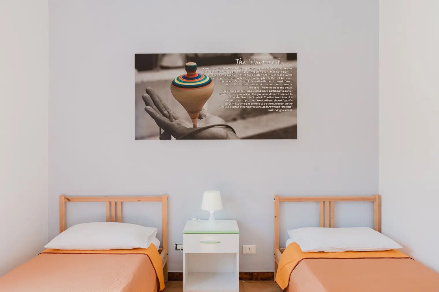A hotel room with two beds, a bedside table with a lamp, and a wall-mounted picture of a hand holding a pottery piece.