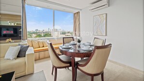 A modern living room with a dining area, large windows, and a city view.