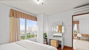 A modern hotel room with a large bed, a desk, a mirror, and a view of the cityscape.