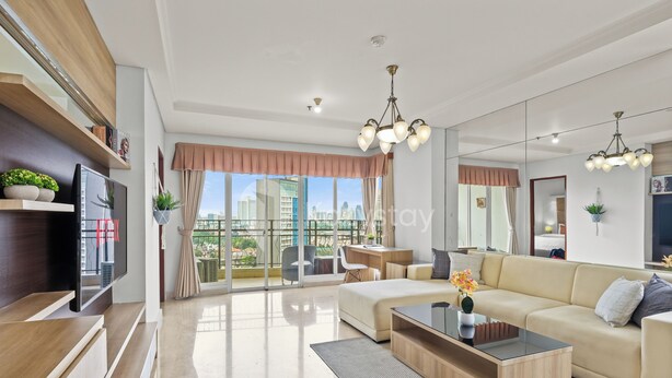 A modern living room with a sofa, coffee table, and TV. There is a balcony with a view of buildings.