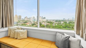 A room with a large window, a yellow cushioned bench, and a view of a cityscape.