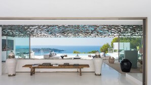 A modern living room with a large window overlooking a scenic ocean view, a wooden coffee table, and a white sofa.