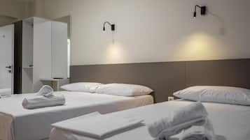A hotel room with two beds, white linens, and towels. There are wall-mounted lights and a door with a mirror.