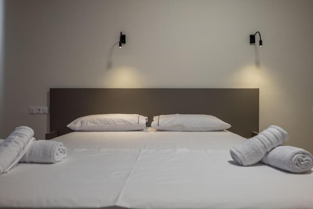 Un letto rifatto con lenzuola bianche e due asciugamani arrotolati su ciascun lato.