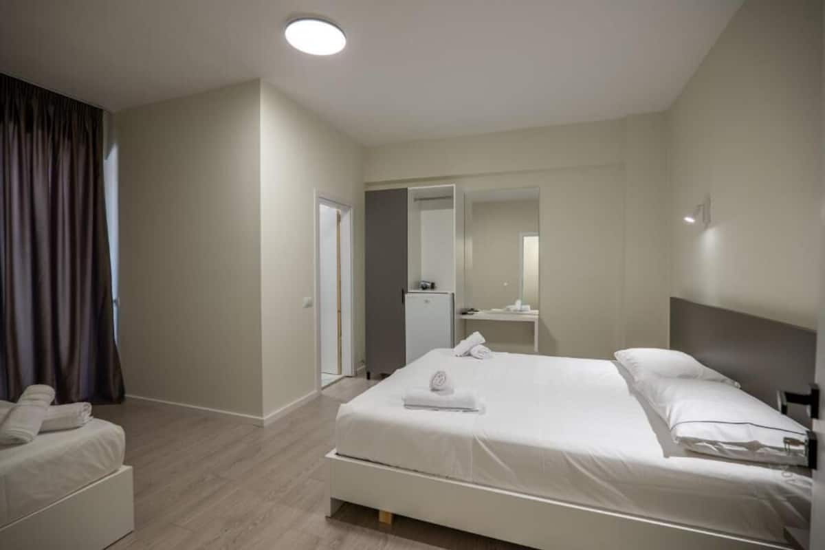 A modern hotel room with a large bed, a bedside table, a mirror, and a wardrobe.