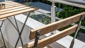 A balcony with a wooden bench and a striped awning, overlooking a pool and greenery. - Meraki Rooms (Sarande)