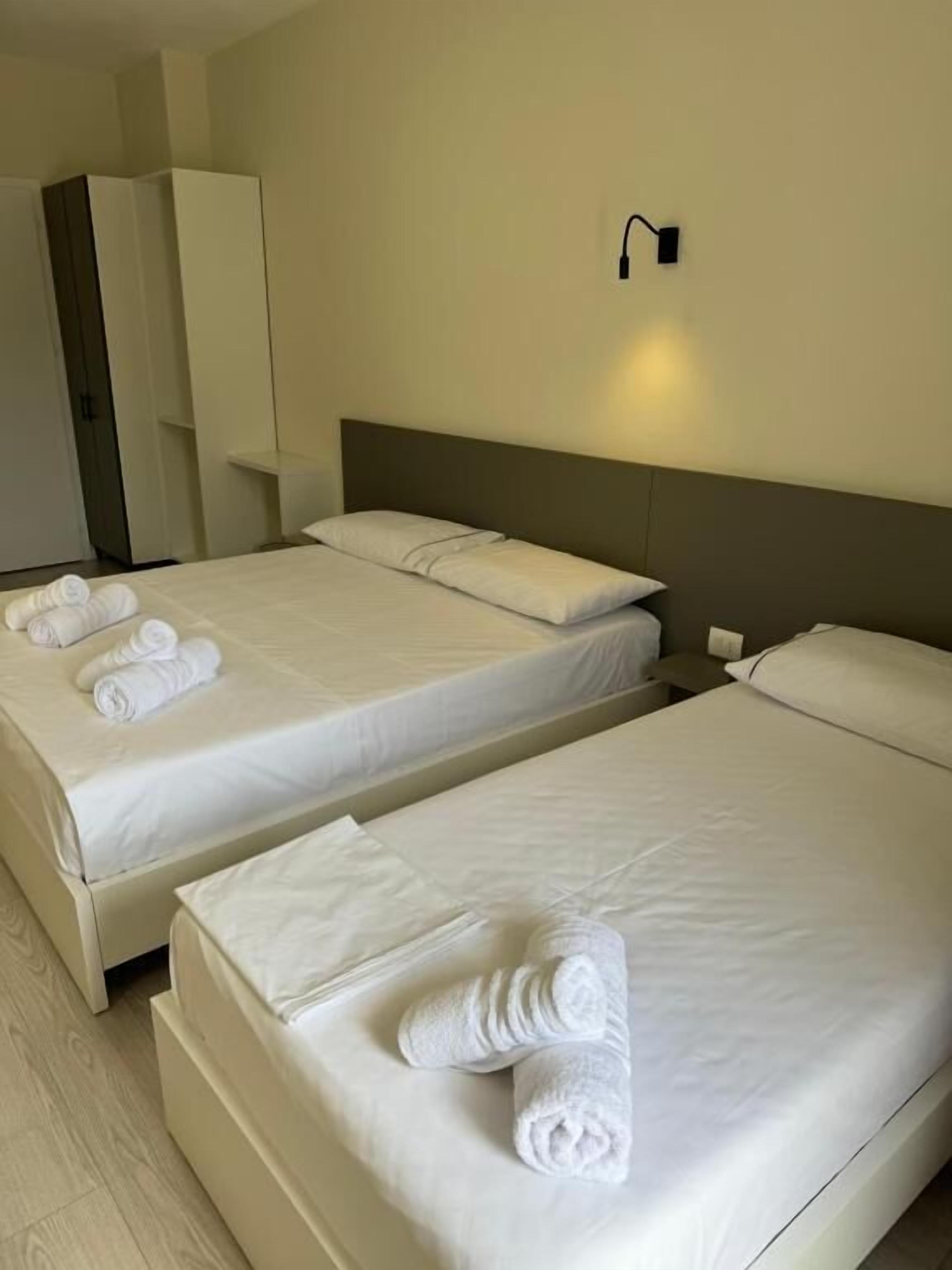 Two single beds with white linens and towels, a wardrobe, and a wall-mounted light fixture.