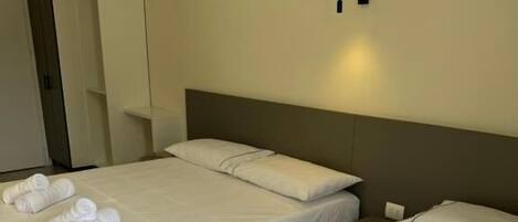 Two single beds with white linens and towels, a wardrobe, and a wall-mounted light fixture.