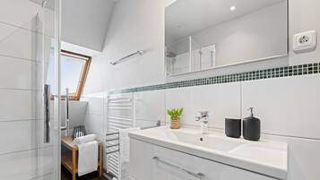 A modern bathroom with a glass shower enclosure, a white sink with black soap dispensers, a towel rack, and a small plant.