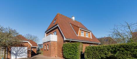 A two-story house with a red-tiled roof, brick walls, and a paved driveway.