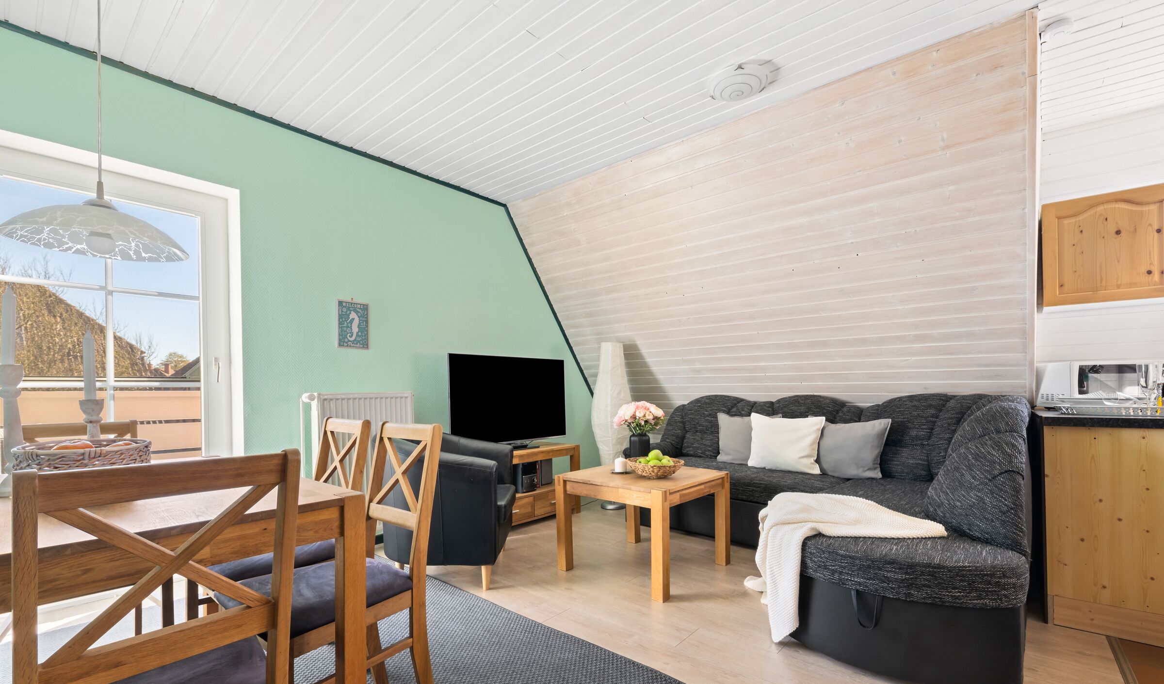 A cozy living room with a sofa, a TV, a wooden dining table, and a window overlooking a scenic view.