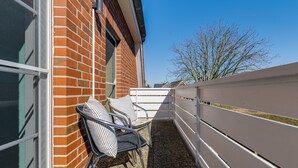 Un balcon avec deux fauteuils en osier, une clôture blanche et un bâtiment en briques.
