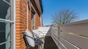 Ein Balkon mit zwei Korbstühlen, einem weißen Zaun und einem Backsteinhaus.