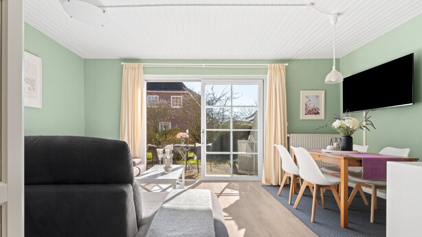 A modern living room with a sofa, a dining table with chairs, a TV, and a sliding glass door leading to a garden.