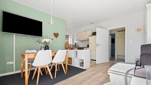 A modern living room with a dining area, a kitchen, and a hallway leading to a bedroom.