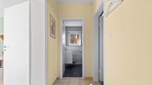 A narrow hallway with a door on the left, a window with blinds in the center, and a door on the right.