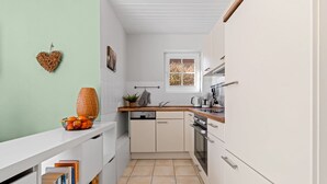 A compact kitchen with white cabinets, a wooden countertop, a built-in dishwasher, and a window with a decorative screen.